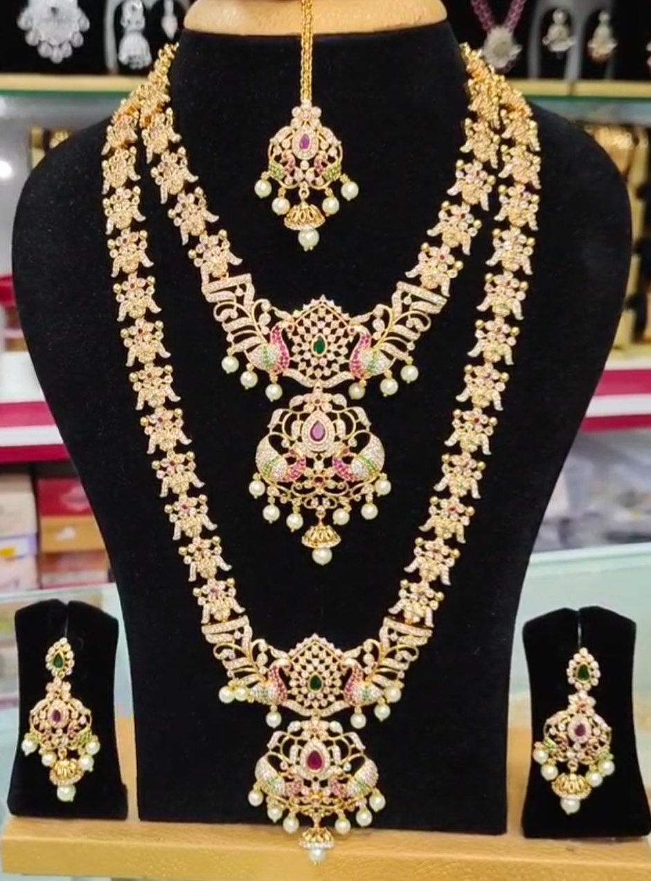 22K gold-plated royal bridal temple necklace set with ruby, emerald, zirconia accents, pearls, and two necklaces (short and long), featuring intricate designs and matching earrings.